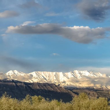Bulutlu mavi gökyüzü altında görkemli kar tepeli dağ ile Kare Manzara doğa görünümü