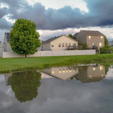 Kare Evler ve ağaçlar çimenli bir arazi ortasında bir göletin parlak su yansıyan