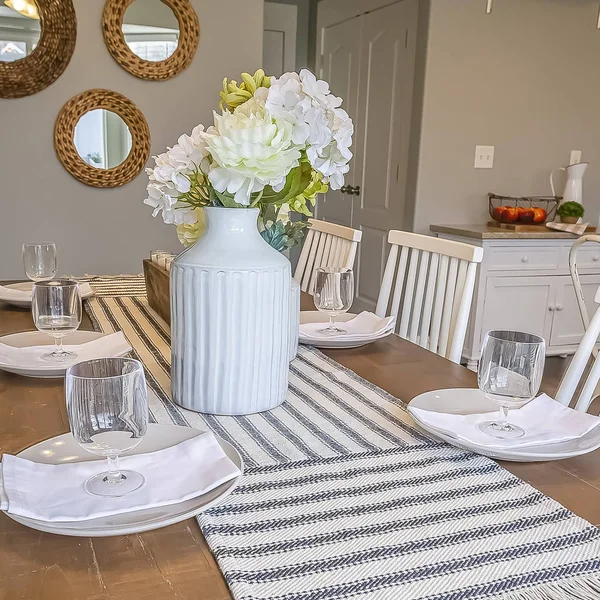 Square frame Table runner flowers glasses napkins and plates arranged on top of dining table