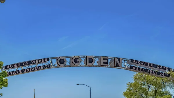 Panorama frame Welcome arch at the city of Ogden in Utah against lush treetops and blue sky