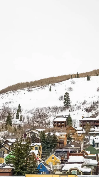 Vertikaler Rahmen riesiger bewölkter Himmel über Häusern, die im Winter auf einem Hügel mit Neuschnee bedeckt sind — Stockfoto