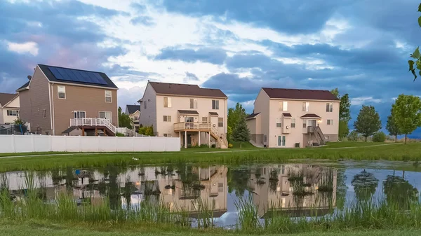 Panorama çerçeve Yeşil metal tezgah evleri ve bulutlu gökyüzü yansıması ile parlak bir gölet bakan