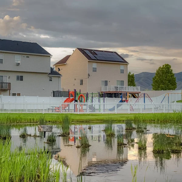 Oyun alanları nın yansıması ile Kare Parlak çimenli gölet bulutlu gökyüzü ve çit