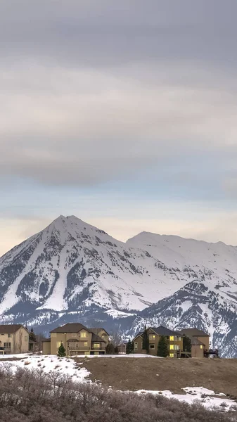 Cadre vertical Maisons avec vue sur la neige imposante sommet de la montagne et ciel couvert en hiver — Photo