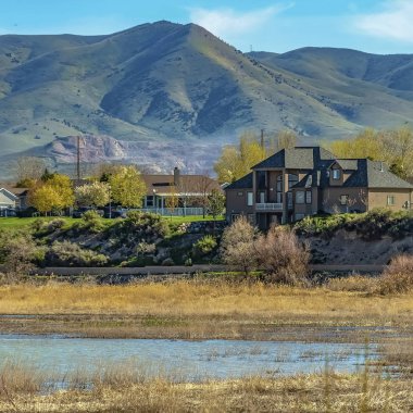 Kare çerçeve Güneşli bir günde dağ ve soluk mavi gökyüzü manzaralı bir göl yakınında inşa edilmiş evler