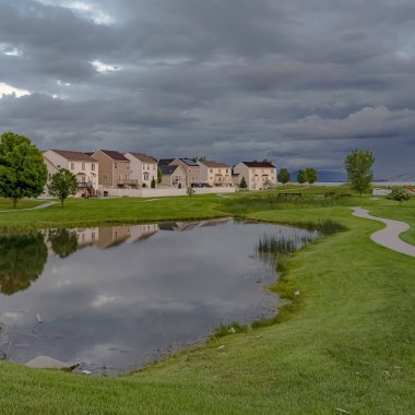Kare çerçeve Bulutlu bir gökyüzü altında parlak bir gölet ve yol ile Manzara mahalle parkı