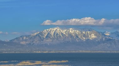 Panorama Kar tepeli dağ ve sakin göl üzerinde kabarık bulutlar ile Canlı mavi gökyüzü