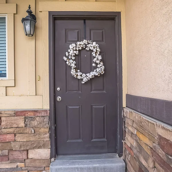 Square White wreath hanging on gray front door of home with a doormat by the doorstep