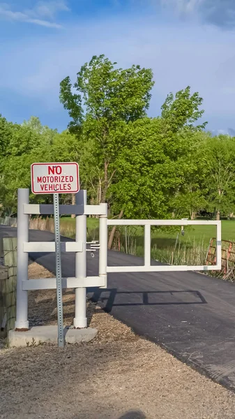 Vertical White gate and sign post on a narrow road with grassy field and trees background