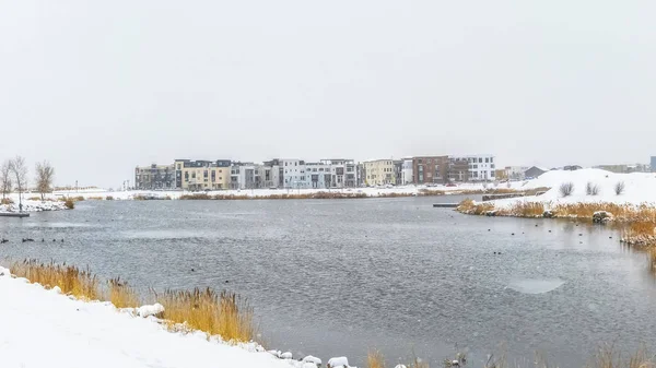 Panorama Lago y edificios rodeados de suelo nevado bajo el cielo nublado en invierno — Foto de Stock