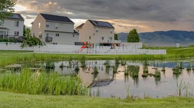 çerçeve Parlak gölet oyun alanı ve çok katlı evler geniş çimenli arazi ile çevrili