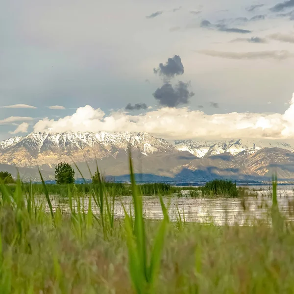 Vierkant schilderachtig uitzicht op de natuur met een glanzend meer en besneeuwde berg onder bewolkte hemel — Stockfoto