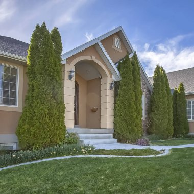 Kare çerçeve Yard ve mavi gökyüzü ve bulutlar altında ev cephesinde konik şekilli ağaçlar