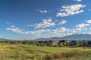 Golf sahası ve güneşli bir günde izlenen göl ve dağ arka plan ile evler