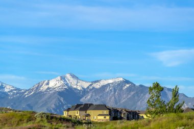 Bulutlu mavi gökyüzüne karşı karlı dağ zirvesine bakan bir tepeüzerinde Evler
