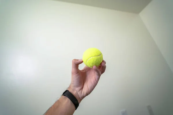 Bola pequeña sostenida por una mano aislada contra una pared blanca y un fondo de techo — Foto de Stock