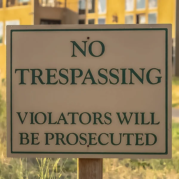 Square frame Close up of No Trespassing sign post beside a paved road that leads to houses — Stock Photo, Image