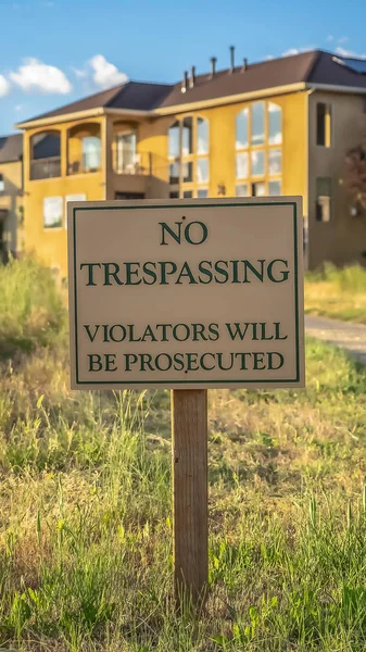 Vertical Close up de No Trespassing sinal poste ao lado de uma estrada pavimentada que leva a casas — Fotografia de Stock