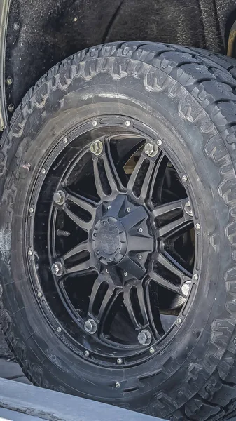 Vertikal ram svart gummihjul av ett silver fordon parkerad på vägen på en solig dag — Stockfoto