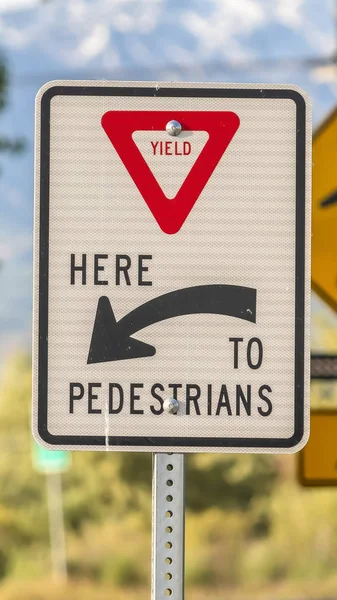 Vertical Yield Here To Pedestrians sign against trees and mountain viewed on a sunny day — Stock Photo, Image