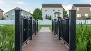 Evlerin önünde bir gölet üzerinde kahverengi güverte ve siyah korkuluklar ile Panorama çerçeve Köprü