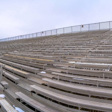 Kışın bulutlu bir gökyüzü altında bir spor arenasında katmanlı banklar Kare çerçeve Satır