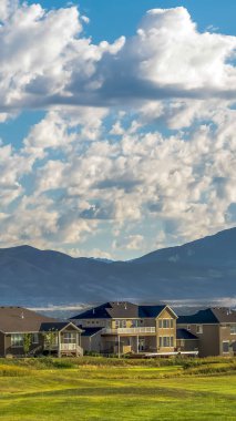Güneşli bir günde bulutlu mavi gökyüzü altında evlerin önünde Dikey Geniş çimenli arazi