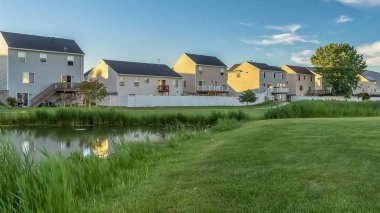 Mavi gökyüzü ve bulutlar altında güzel aile evleri önünde Panorama çerçeve Pond ve yemyeşil alan