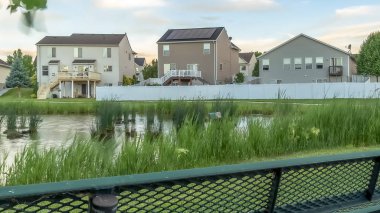 Bulutlu gökyüzü altında çimenli gölet ve evler manzaralı Panorama Yeşil metal park tezgah