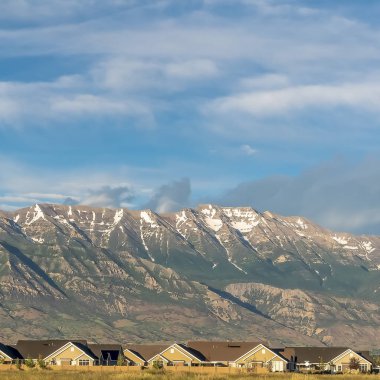 Güneşli bir günde evler ve geniş çimenli arazi üzerinde yükselen Kare Muhteşem dağ