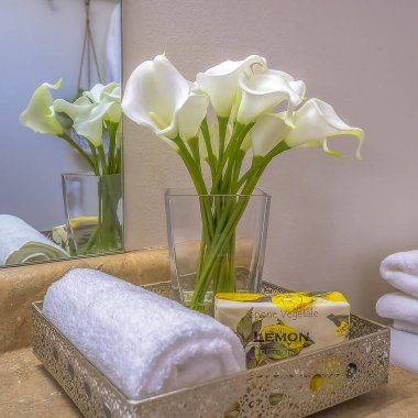 Banyo makyaj tezgahının üstüne yerleştirilen havlu çiçekleri ve sabunlu kare çerçeveli tepsi