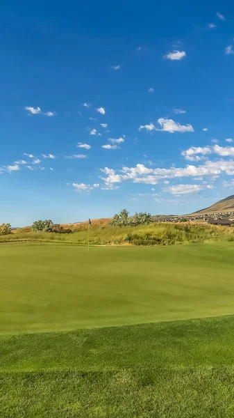 Vertikal umrahmter Golfplatz mit lebhaft grünem Fairway unter blauem Himmel und Wolken an einem sonnigen Tag — Stockfoto