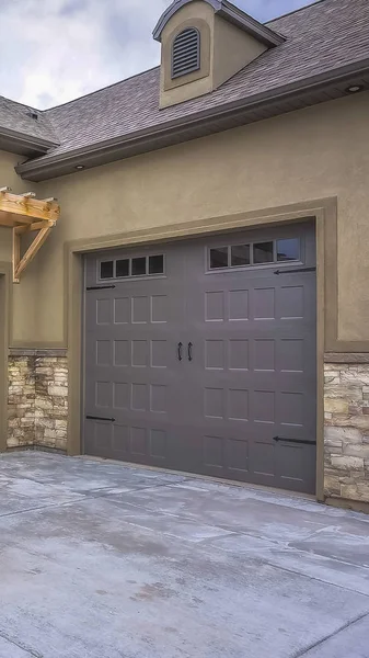 Vertical Exterior of a home with view of gray double garage doors and stone wall