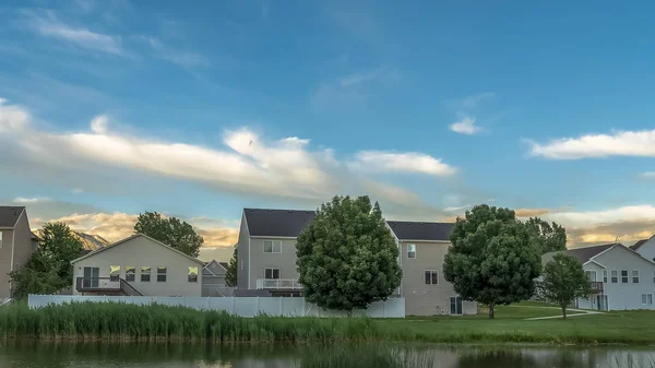 Marco panorámico Camino a lo largo de un estanque brillante en un terreno herboso con casas en el fondo — Foto de Stock