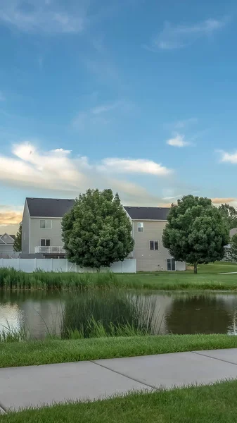 Quadro vertical Caminho ao longo de uma lagoa brilhante em um terreno gramado com casas no fundo — Fotografia de Stock