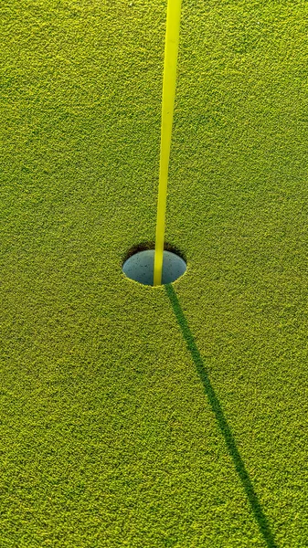 Vertical frame Green of a golf course with close up view of the yellow flagstick and hole — Stock Photo, Image