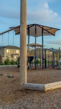 Dikey çerçeve Slaytlar ve evler dağ ve bulutlu mavi gökyüzüne karşı bir parkta salıncaklar