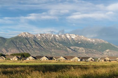 Güneşli bir günde evler ve geniş çimenli arazi üzerinde yükselen muhteşem dağ