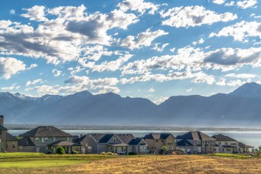 Bulutlu mavi gökyüzü altında göl ve dağ manzaralı yerleşim alanı