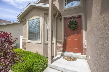 Güneşli bir günde bir evin girişinde çelenk ile dekore kahverengi ön kapı