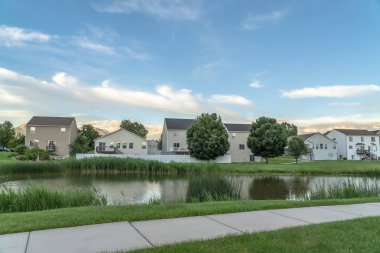 Arka planda evleri ile çimenli bir arazi üzerinde parlak bir gölet boyunca Pathway