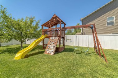 Sarı plastik kaydırak salıncakları ve tırmanma duvarı ile ahşap oyun alanı yapısı