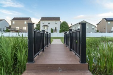 Evlerin önünde bir gölet üzerinde kahverengi güverte ve siyah korkuluklar ile Köprü