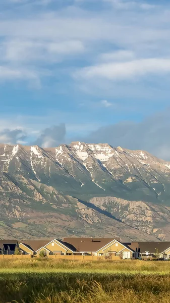 Marco vertical Magnífica montaña que se eleva sobre las casas y el vasto terreno herboso en un día soleado —  Fotos de Stock