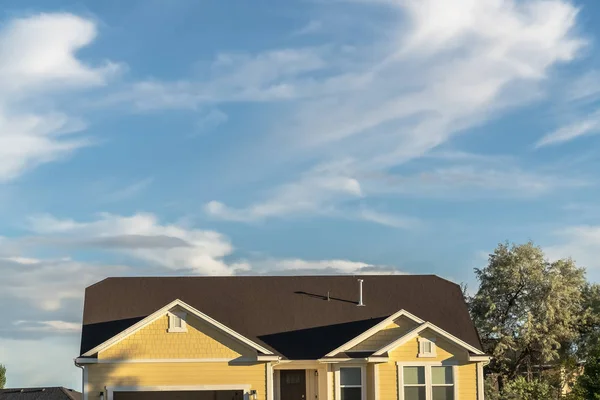Снаружи дома с темной крышей и кремовой стеной на фоне солнечного облачного голубого неба — стоковое фото