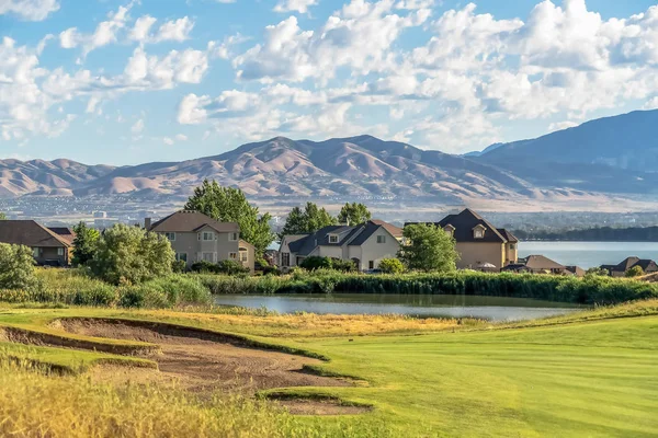 Güneşli bir günde dağ ve bulutlu mavi gökyüzüne karşı bir gölet ve göl yakınındaki evler