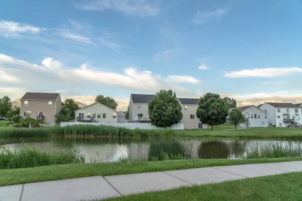 Arka planda evleri ile çimenli bir arazi üzerinde parlak bir gölet boyunca Pathway