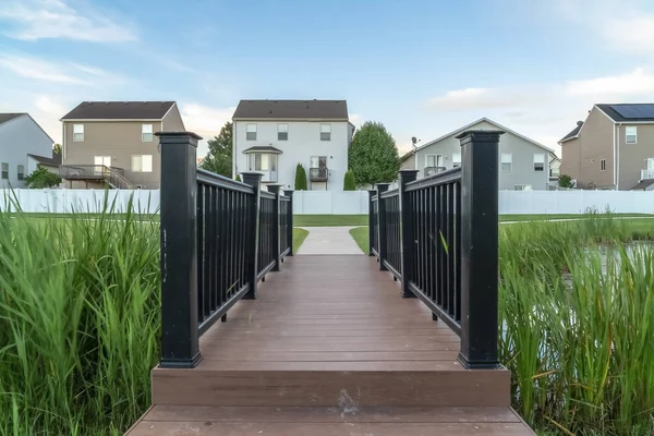 Evlerin önünde bir gölet üzerinde kahverengi güverte ve siyah korkuluklar ile Köprü