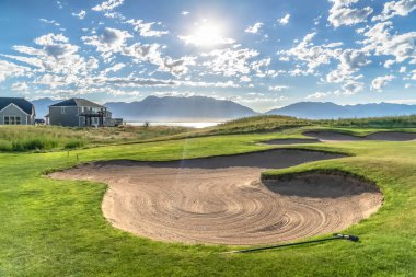 Bir golf sahası nın kum sığınağı ve gökyüzündeki parlak güneşin ve kabarık bulutların görünümü