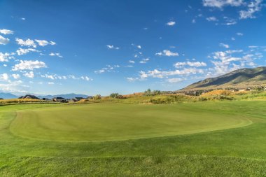 Güneşli bir günde mavi gökyüzü ve bulutlar altında canlı yeşil fairway ile Golf sahası